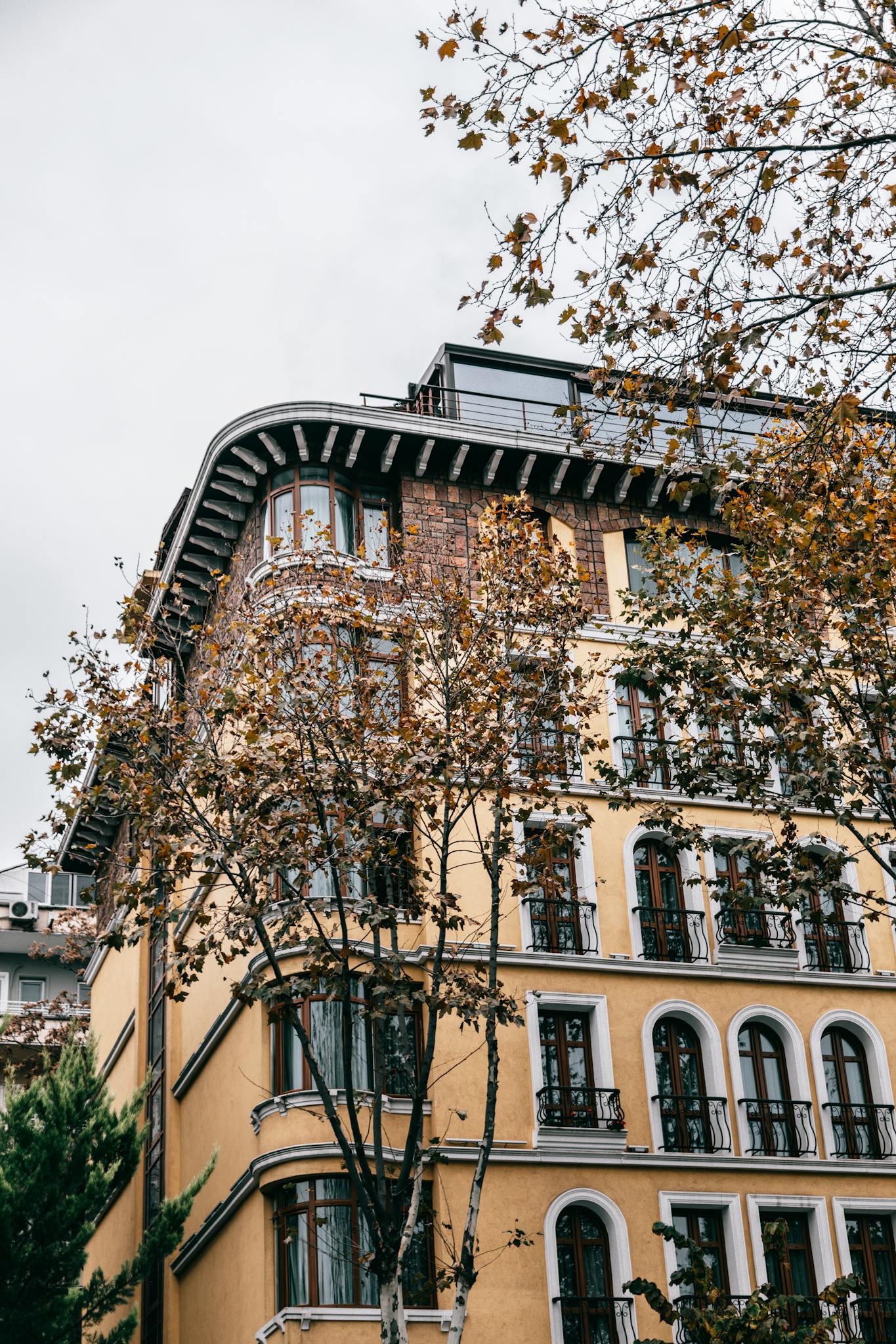 Corner of brown aged residential building with widows of different shapes on autumn day