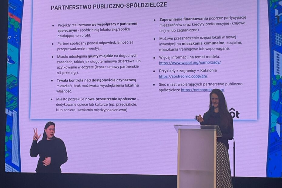 Joanna Marcinkowska prezetuje ideę cohousingu senioralnego na scenie Centrum Kreatywności Targowa, za nią wyświetlana jest prezentacja.